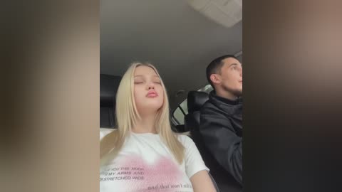 Media: Video of two people in a car: a blonde woman with straight hair and a white shirt, and a man with short black hair and a black jacket, looking forward.