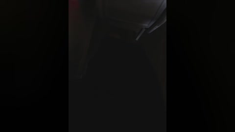 A dimly lit video of a person's head, partially obscured by a dark hat, with shadows creating a mysterious, noir-like atmosphere. The background is almost entirely black, enhancing the enigmatic mood.