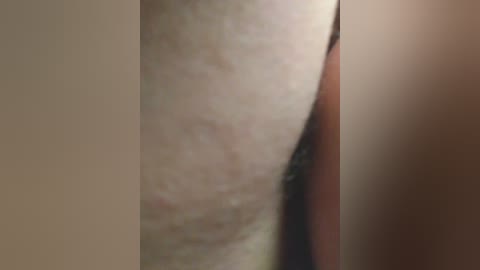 Video of a close-up, side view of a person's pale, slightly hairy thigh with faint moles. The background is blurry and beige.