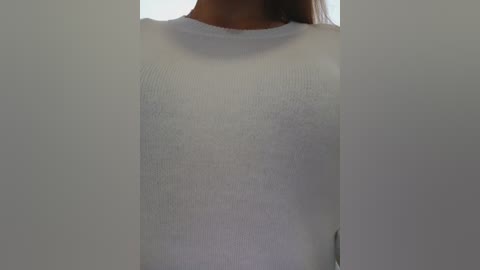 A close-up video of a person wearing a white, ribbed, long-sleeved sweater. The image is cropped to show only the upper torso, with the lower half and face obscured by the sweater's texture.
