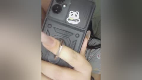 Video of a person holding a smartphone with a panda sticker case, showing a partially visible erect penis. The background includes a blurred, light-colored shirt and a hand with a silver ring.