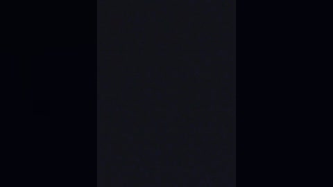 A dimly lit video shows a vertical black object against a dark background, creating a minimalist, moody atmosphere with an abstract, enigmatic feel.
