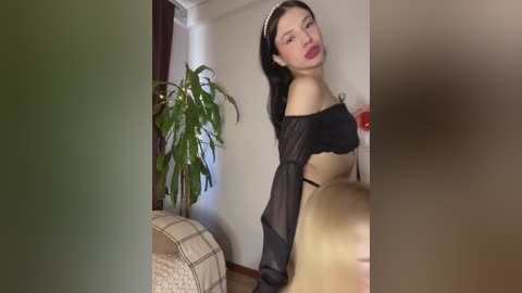 Video of a young Asian woman with fair skin and long black hair, wearing a sheer black off-shoulder top and black panties, posing seductively indoors.