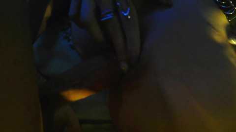 A dimly-lit, close-up video of a hand with a ring touching a woman's vulva, visible in shadowy light.