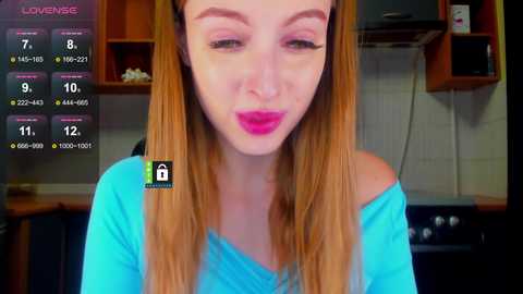 A video of a fair-skinned woman with long, straight, light brown hair and pink lipstick, wearing a turquoise off-shoulder top, in a modern kitchen with wooden cabinets and a stove.