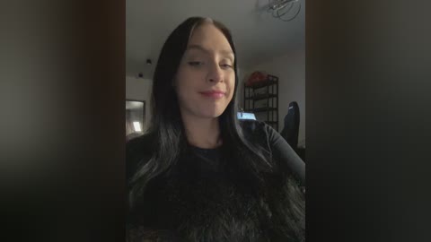 A video of a young woman with long black hair, wearing a black sweater, indoors, slightly out of focus.