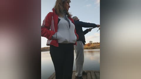 Media: A video shows a middle-aged woman in a red jacket and a man in a dark jacket on a wooden dock, gazing at a serene lake under a partly cloudy sky.