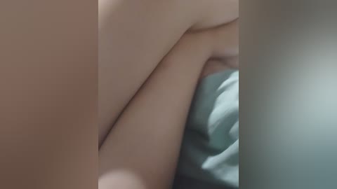 A close-up video of a light-skinned person lying on a bed with a teal-colored sheet, showcasing their bare upper body, with a soft, blurred background.