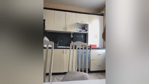 Media: A video of a small, modern kitchen with light-colored cabinets, a black backsplash, and a white chair, featuring a red bowl on a countertop.