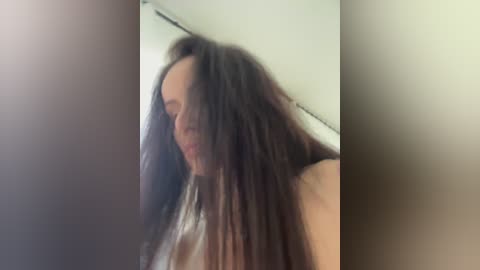 Media: Video of a woman with long, dark brown hair and pale skin, blurred in the background, possibly in a bathroom.