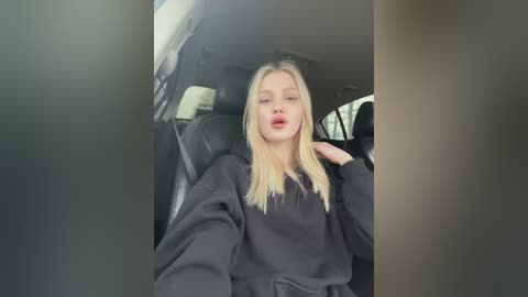 Media: A video of a young, fair-skinned woman with long, straight blonde hair, wearing a black hoodie, sitting in the driver's seat of a car.