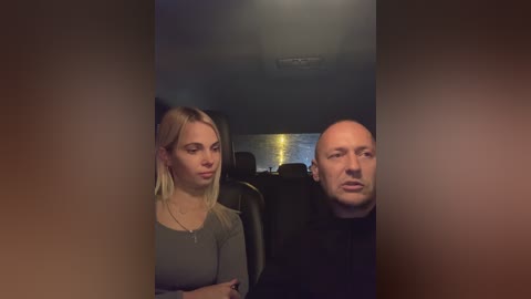 Media: Video of a young woman with long blonde hair in a grey top and a bald man in a black shirt sitting side by side in a dimly lit car.