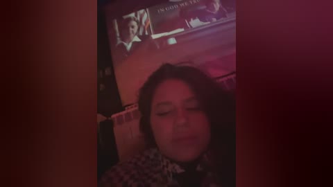 Video of a woman with closed eyes, lying on a couch, surrounded by dim lighting, with a TV screen displaying a news anchor in the background.