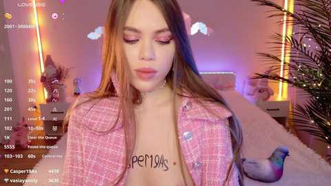Media: Video of a young woman with light skin, long brown hair, wearing a pink tweed jacket and a choker, in a pink room with a bed and plant, with a live stream overlay.