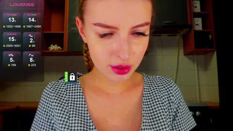 A video of a young woman with light skin and brown hair, wearing a checkered blouse, captured in a dimly lit kitchen with a \"LoveMeter\" screen displaying her emotional state.