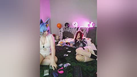 Video of a bedroom with two women in cat costumes, one with blue hair, the other with red hair, surrounded by Halloween decorations and a messy bed.