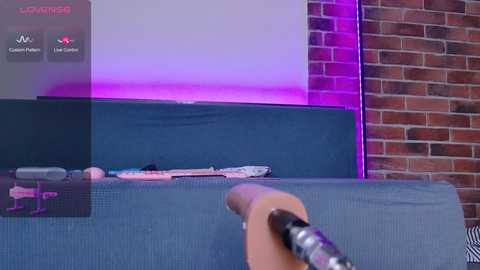 Video of a hand holding a controller in front of a TV mounted on a brick wall, displaying a game with a purple background.