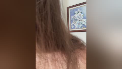 Media: A close-up video of a person's long, light brown hair, partially obscuring a light-skinned face. The background features a framed painting of white lilies on a beige wall.