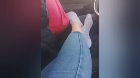 Video of a person's legs, wearing light gray socks and blue jeans, reclined in a car seat with a red shirt visible.