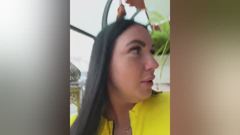 A video of a woman with long black hair, wearing a yellow shirt, being lifted by two men. Background shows blurred greenery and a metal railing.