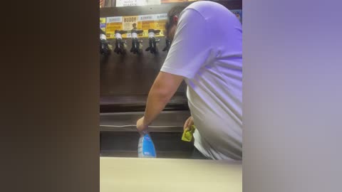 Media: A video captures a man in a white t-shirt, bending over to refill a blue bottle at a soda fountain, with a blurry background of vending machines and signage.