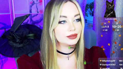 A video of a blonde woman with blue eyes, wearing a black choker and red lipstick, in a dimly lit room with purple lighting.