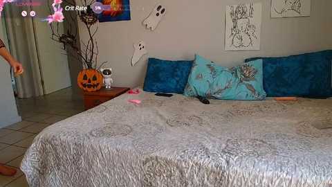 A video of a messy bedroom with a beige quilted bedspread, blue pillows, a carved pumpkin, and scattered items.