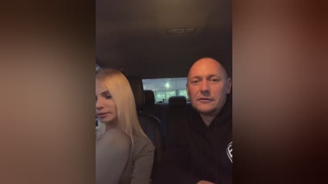 Media: A video captures a man with a shaved head and a woman with long, straight blonde hair seated in a car. Both appear calm, with the woman looking away.