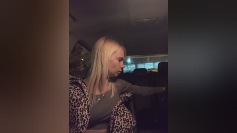 Media: Video of a blonde woman in a leopard-print jacket, sitting in a dimly lit car, with blurred background and shadowy interior.