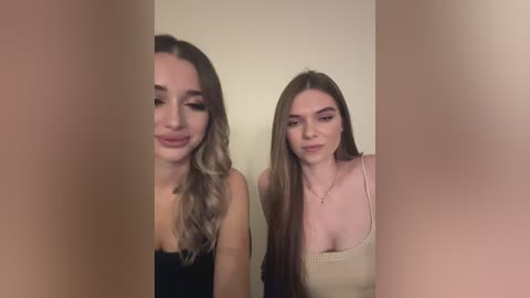 Media: A video of two young women with long, straight hair, one in a black top and the other in a beige tank, smiling against a plain, off-white wall.