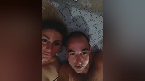 Media: Video of a topless woman with dark hair and a man with bald head, lying on a bed with Gucci-patterned pillows.