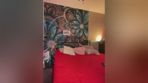 Video of a bedroom with a bed covered in red sheets, adorned with a vibrant, detailed blue and teal floral mural on the wall. A small lamp and a TV are visible in the background.