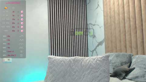 Video of a modern living room with light gray walls, textured pillows, vertical black and white stripes, beige curtains, and a digital clock display on the left.