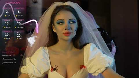 Media: A video of a woman in a white, puffy-sleeved wedding dress with a veil, standing against a dimly lit background. She has blue eye makeup and a sad expression.