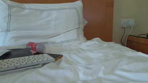 Video of a bed with white sheets and pillows, a laptop, and a red drink can on the bed, against a wooden headboard and beige wall.