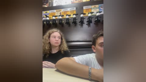 Media: Video of a girl with curly blonde hair and a boy with short brown hair in a fast-food restaurant, both seated at a table. Background features a counter with toy figurines and a menu board.