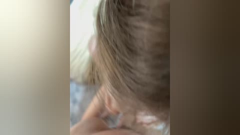A close-up video of a woman's back and shoulder, showing light blonde hair, partially obscured by a blurry background, suggesting an intimate, possibly private setting.