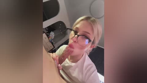 Media: Video of a blonde woman with glasses performing oral sex on a large, erect penis in a dimly lit room.