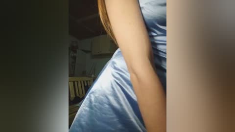 Video of a woman's arm in a light blue satin sleeve, in a dimly lit bedroom with a wooden crib and a white cabinet in the background.