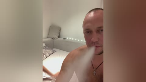 Media: A video of a bald, shirtless man with a cross necklace, smoking a cigarette, standing in a dimly lit bathroom with a white bathtub, gray towel, and beige wall.