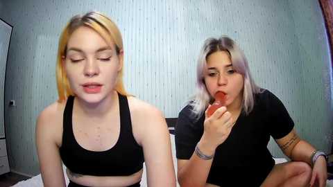 Media: A video of two young women in casual attire, one blonde and one with dyed hair, eating a strawberry.