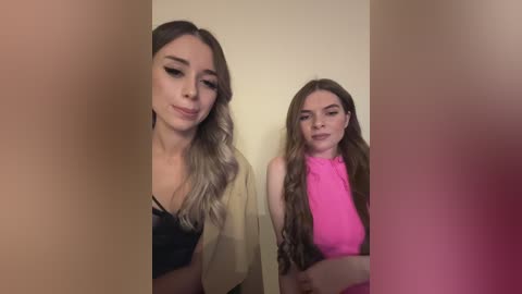 Media: Video of two young women with long, wavy hair, one in a beige top, the other in a pink top. Both have fair skin and are smiling. Background is blurred, focusing on their faces.