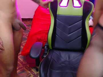 Video of a gaming setup with a gamer chair featuring a green and black design, surrounded by a carpeted room with red and orange objects, and a partially visible male figure.