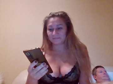 Video of a middle-aged Caucasian woman with long blonde hair, wearing a black lace bra, taking a selfie with a smartphone, in a dimly lit bedroom.