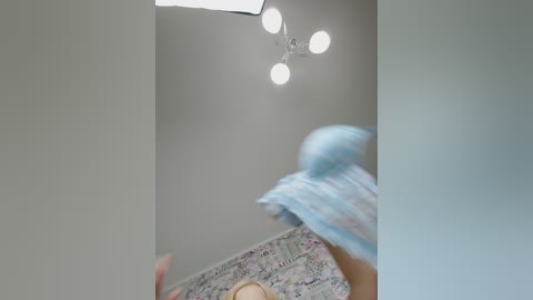 Media: Video of a child in a blue and white dress, playing with a toy in a bright, modern room with a patterned carpet, a white ceiling, and a light fixture with four bulbs.