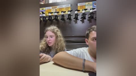 Media: A video of two young women with curly hair, sitting in a dimly lit room with a counter and a row of drink dispensers in the background.