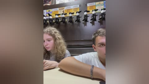 Media: A video of two young people sitting side by side at a table, with a background of mounted microphones and colorful signs in a dimly lit room.