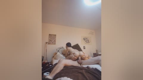 Video of two naked people on a bed, a man and a woman, engaged in sexual activity. The room has beige walls with minimalistic decor.
