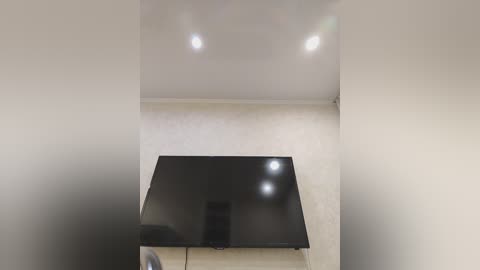 A minimalist, modern living room with a large, flat-screen TV mounted on a sleek, light wood cabinet against a plain beige wall. The room features a neutral color palette, clean lines, and soft lighting.