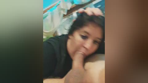 Video of a young Asian woman with dark hair, wearing a black top, performing oral sex on a man. She is in a bedroom with a blue bedspread.